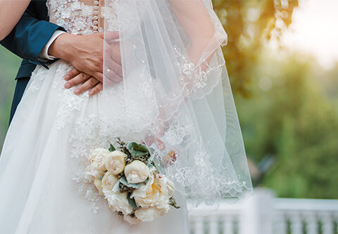 Newly married couple. Wedding day. Bouquet of the bride in the hands, the groom's embrace. Free space.